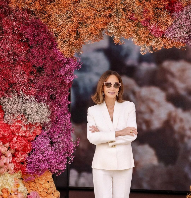 a woman in a suit and glasses staying bellow some sort of flower structure looking at you